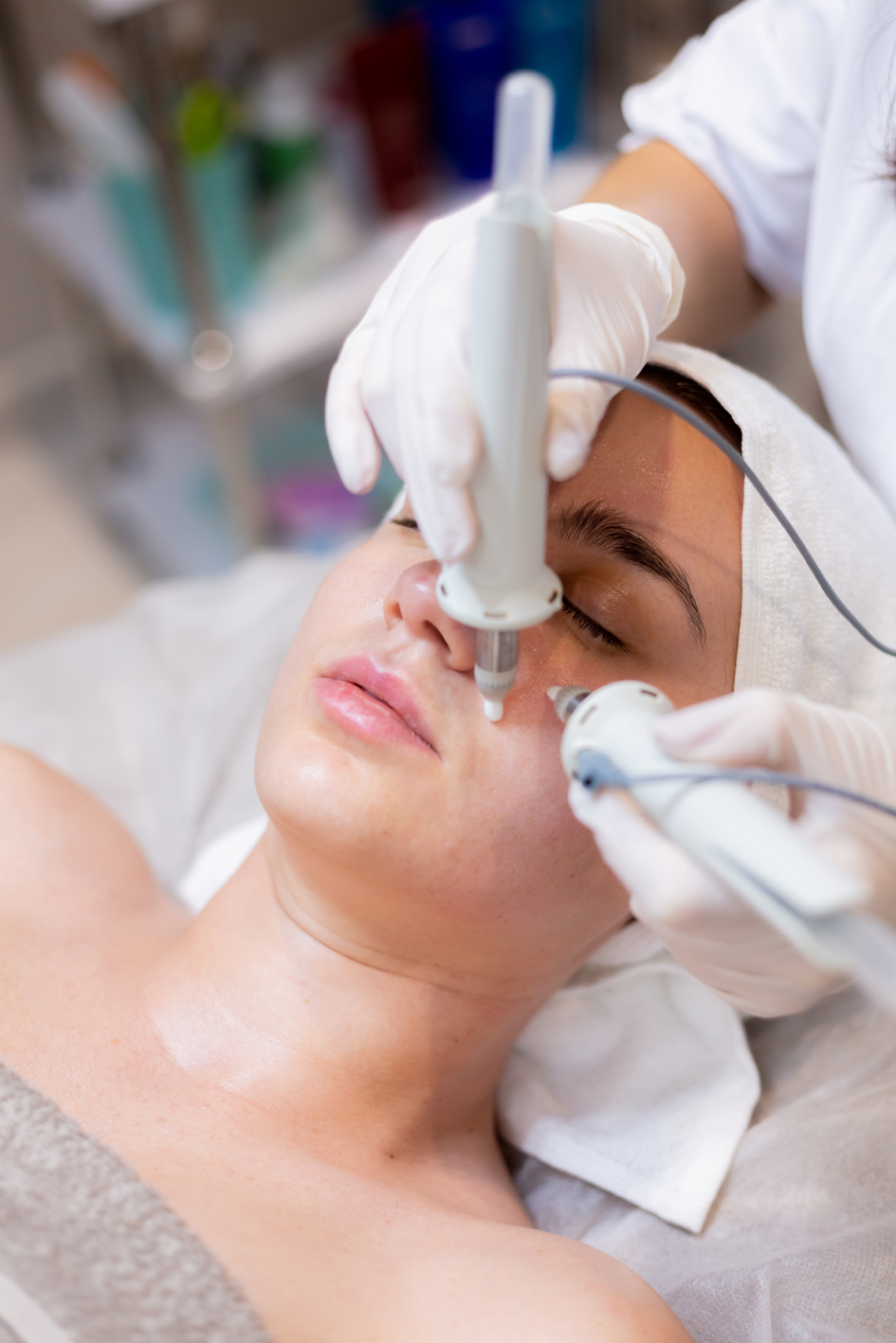 A young beautiful girl lies on the beautician's table and receives procedures with a professional apparatus for skin rejuvenation and moisturizing